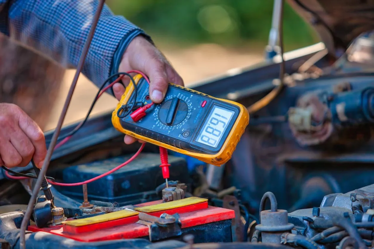 Auto electrician testing a vehicle battery with a multimeter